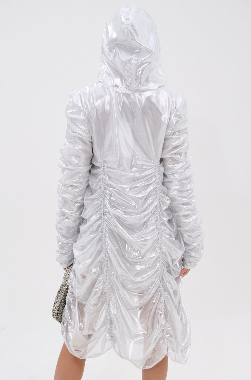 A person is seen from behind against a plain white background wearing the WAYS TO GO METALLIC ADJUSTABLE DRESS IN WHITE, featuring ruched detailing down the back and a hood, while holding a small, textured handbag.