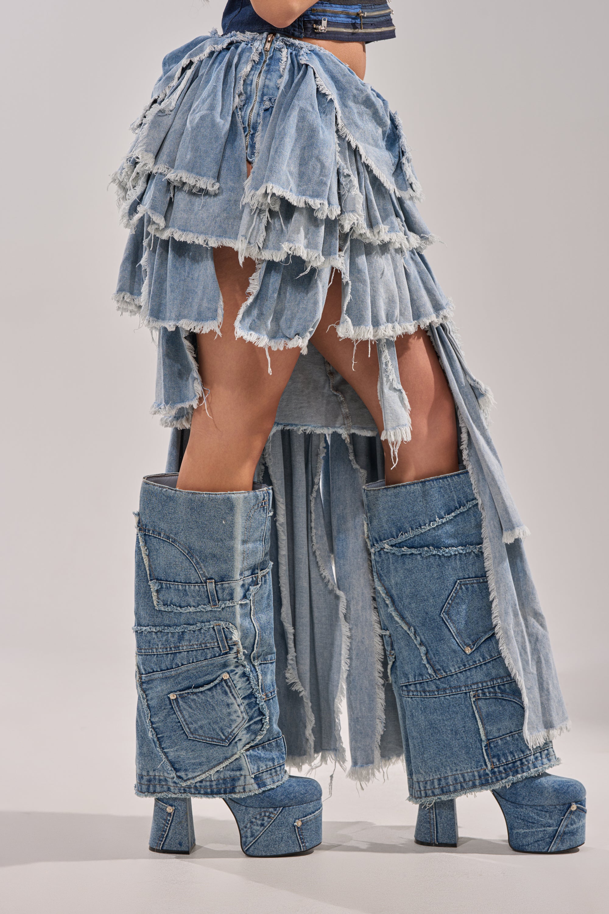 Person wearing the DISTRESSED TIERED ASYMMETRIC MIDI SKIRT paired with chunky, high platform patchwork denim boots, standing against a plain background. 5