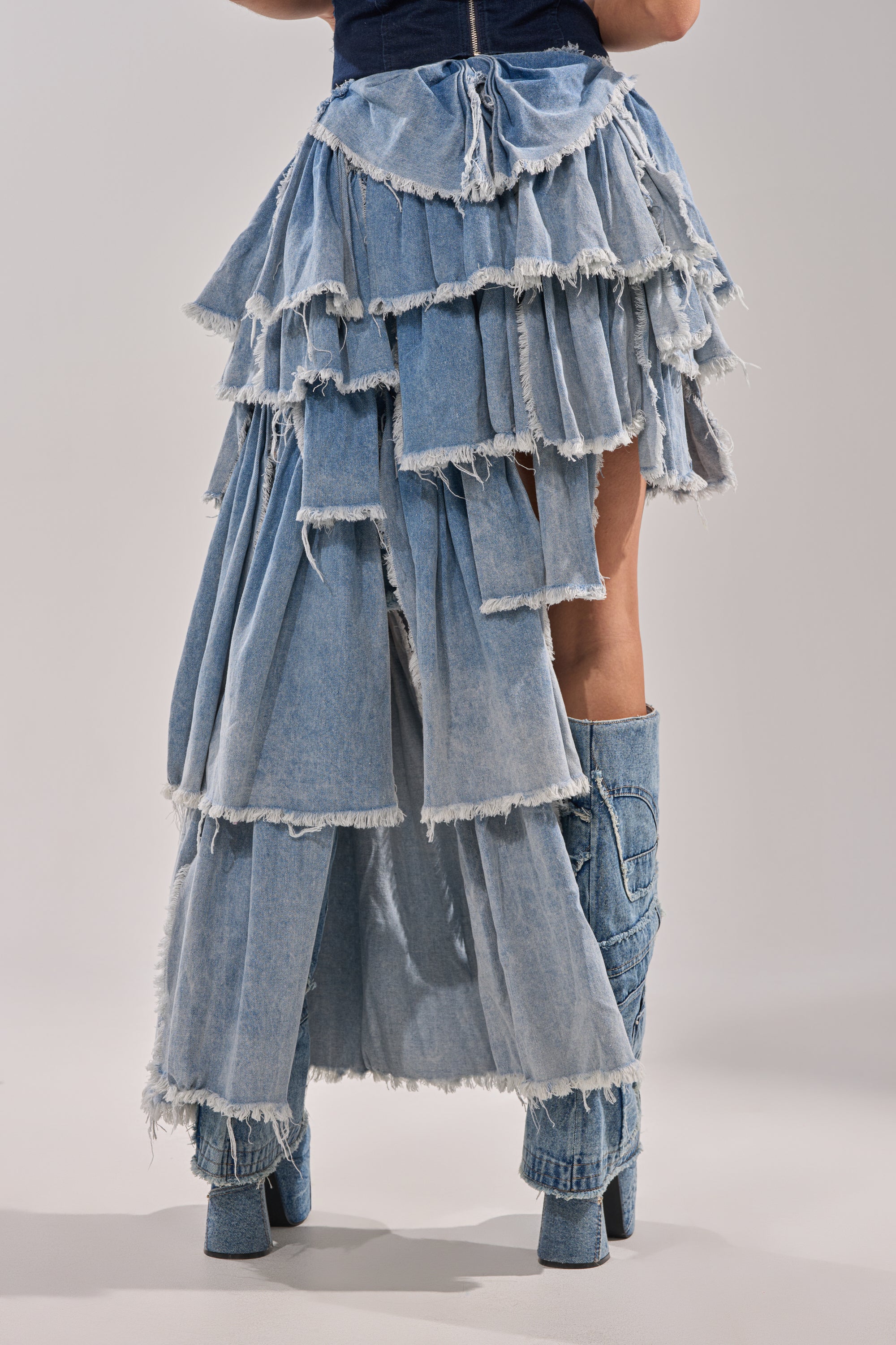 A model showcases the DISTRESSED TIERED ASYMMETRIC MIDI SKIRT and matching denim boots, shot from the waist down against a plain background. 6