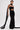 A person stands confidently in the READY FOR A NIGHT OUT LACE MAXI DRESS, featuring sheer panels and a long matching scarf, showing off tattoos and styled with slicked-back hair and bold earrings.