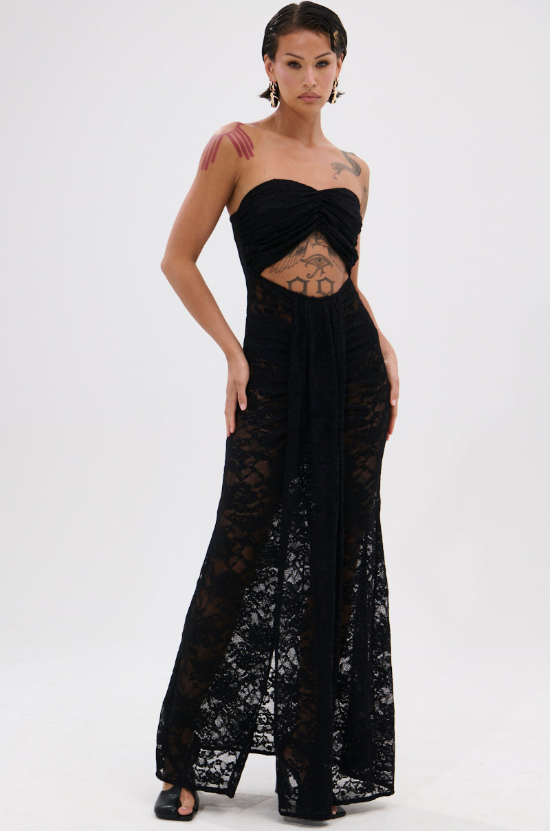 Confidently posed, a person wears the READY FOR A NIGHT OUT LACE MAXI DRESS—a strapless black sheer lace column maxi featuring a midriff cutout. Slicked-back hair and tattoos add edge to the bold look.