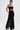 Confidently posed, a person wears the READY FOR A NIGHT OUT LACE MAXI DRESS—a strapless black sheer lace column maxi featuring a midriff cutout. Slicked-back hair and tattoos add edge to the bold look.