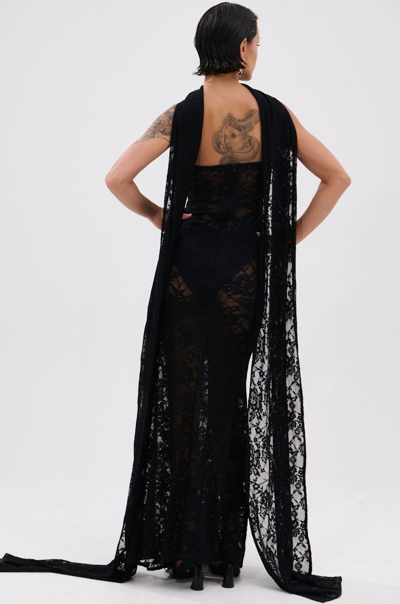A person with short dark hair and visible back tattoos models the READY FOR A NIGHT OUT LACE MAXI DRESS with a matching draped scarf, standing against a plain white background and facing away from the camera.