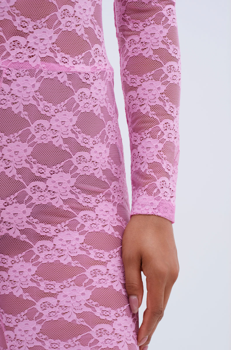 A close-up of an arm and hand wearing the FROM DAY TO NIGHT LACE JUMPSUIT IN LIGHT PINK, featuring long sleeves and a delicate pink floral lace. The background is plain and light-colored.