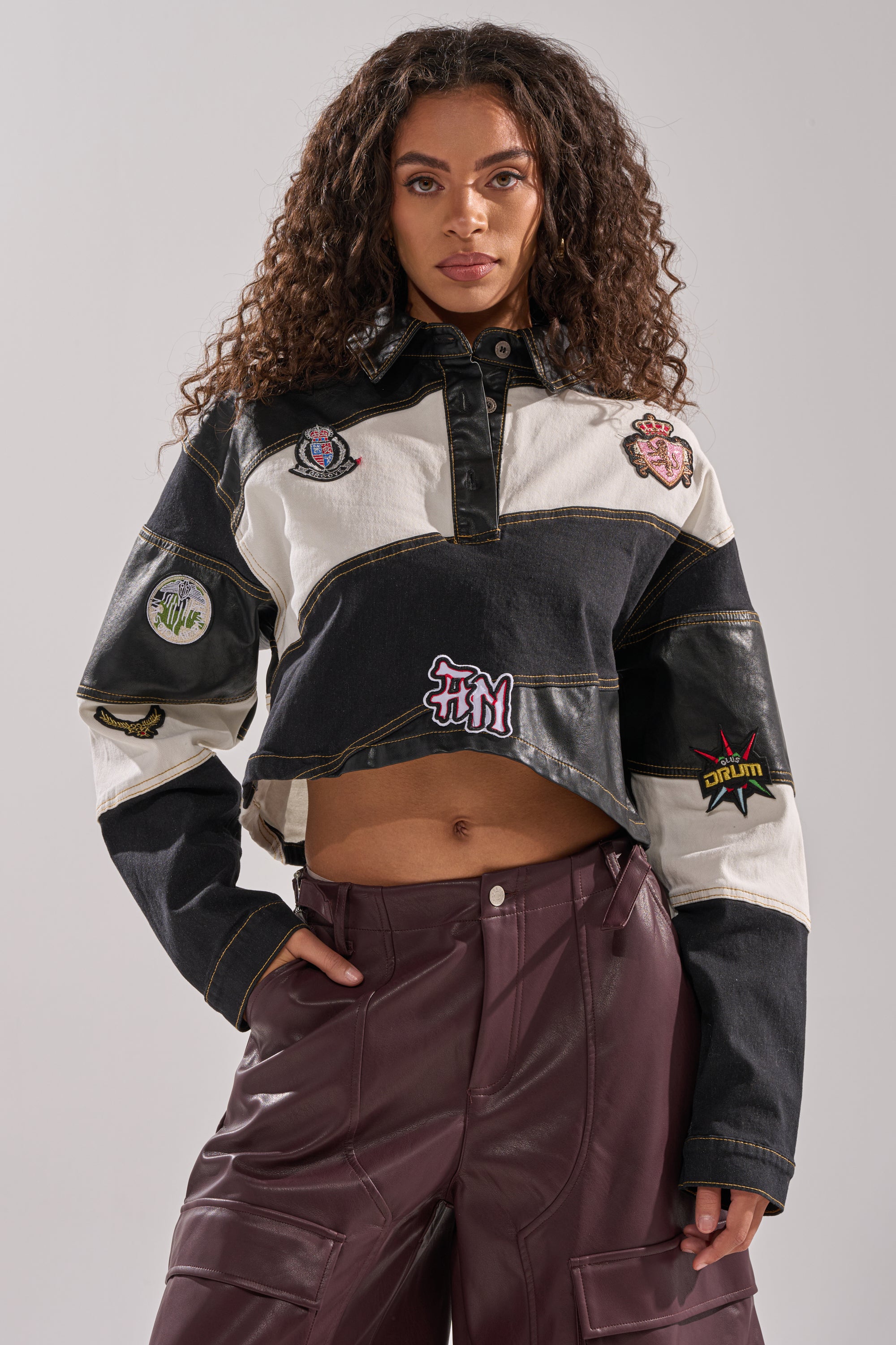 A woman with long curly hair wears the GUESS WHAT STRIPE COLLARED BLOUSE, standing confidently against a plain light gray background.