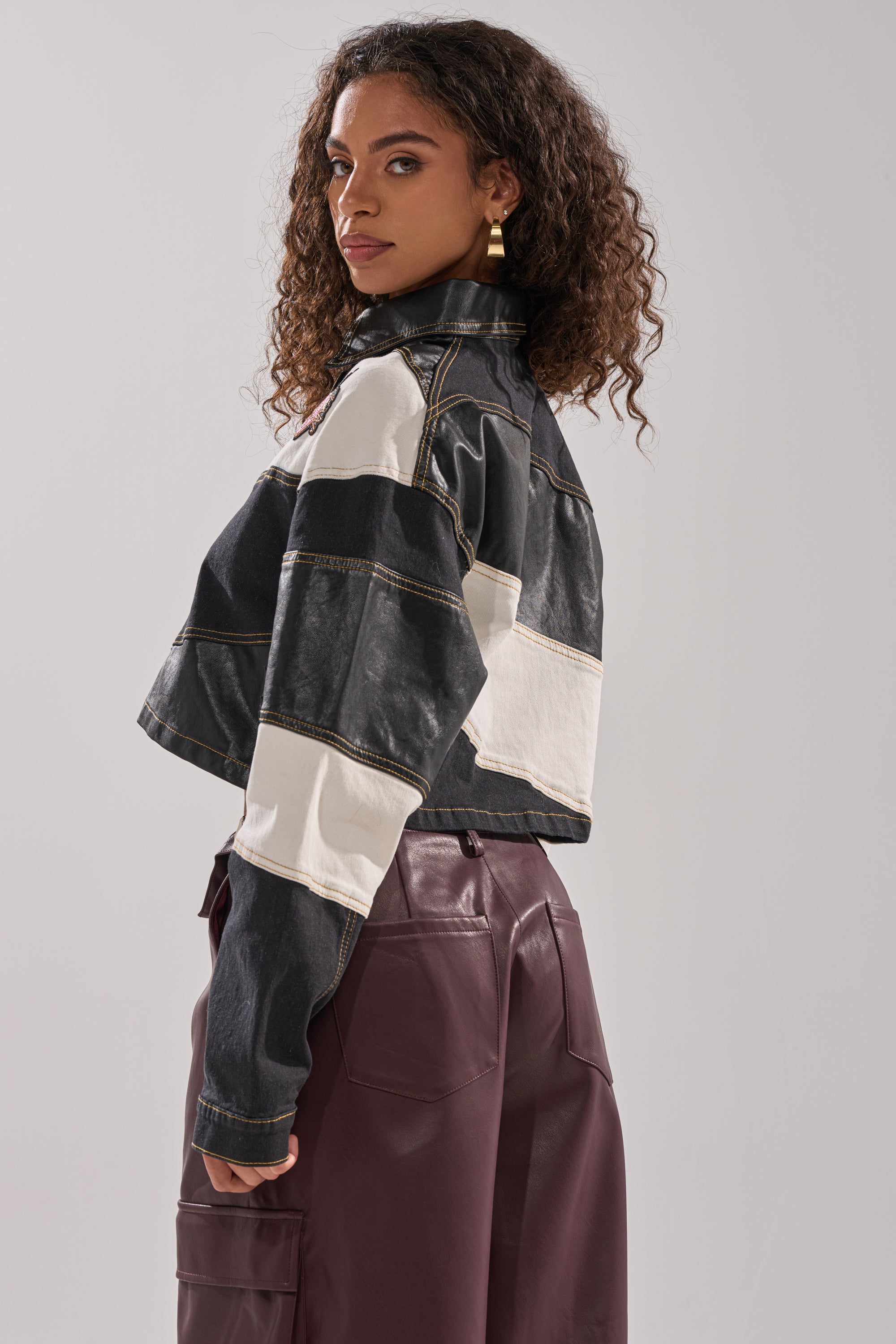 A woman with curly hair stands sideways, wearing the GUESS WHAT STRIPE COLLARED BLOUSE, looking over her shoulder against a plain light background.