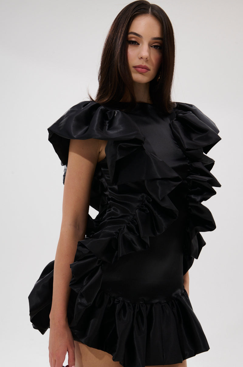A woman with long dark hair, in THE MOMENT IS MINE SATIN MINI DRESS, stands against a plain light background and gazes to the side with a neutral expression.