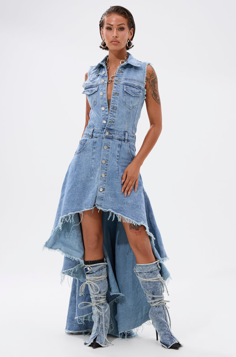 A woman models the READ IT AND WEEP DENIM MINI DRESS, featuring a light-wash finish, frayed edges, front buttons, and multiple pockets. She completes the look with matching denim boots against a plain white background.