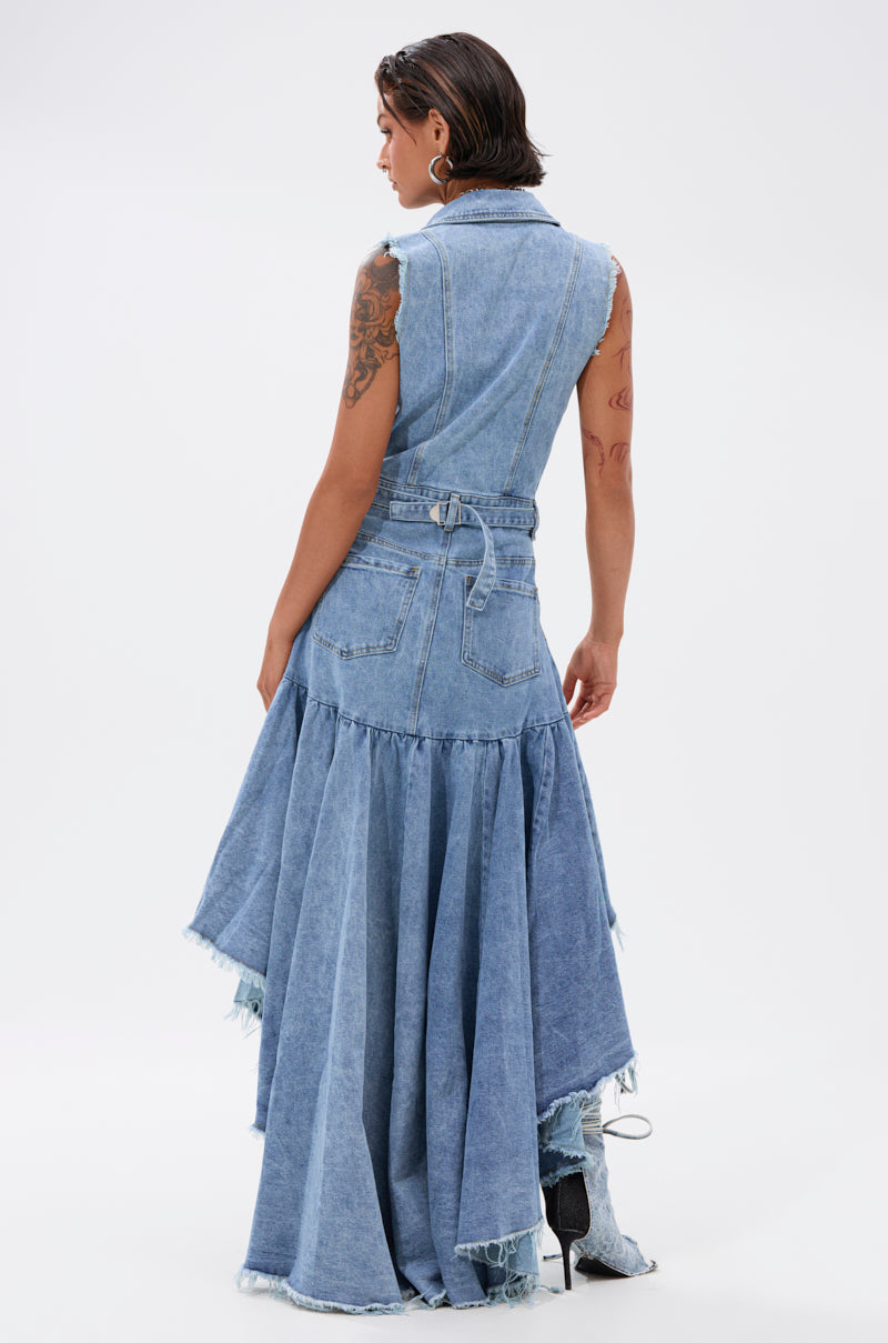 A person with short, wet-look dark hair models the READ IT AND WEEP DENIM MINI DRESS—a sleeveless, light-wash piece with a belted waist and flared, asymmetrical ruffled hem—shown from the back against a plain white background.