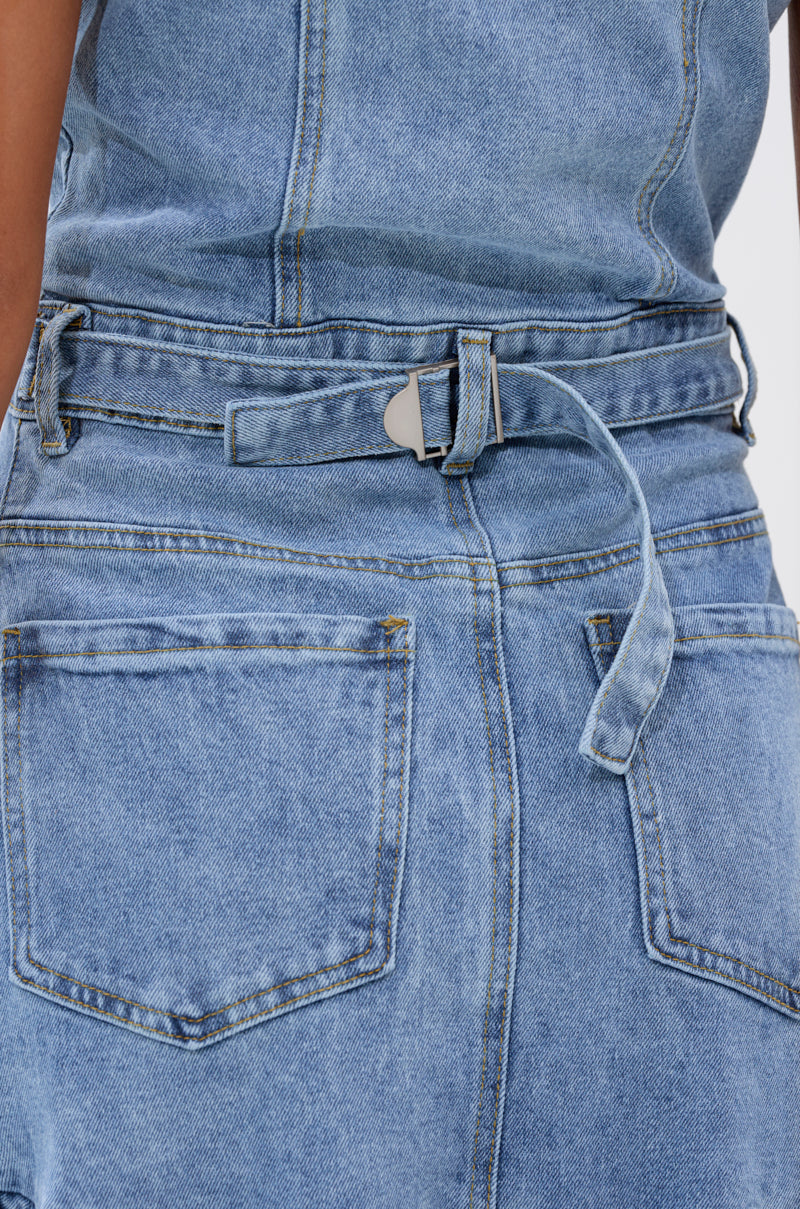 Close-up of the READ IT AND WEEP DENIM MINI DRESS, a light-wash mini dress with a belted waist, visible seams, back pockets, belt loops, and a ruffled hemline for a playful touch on classic denim.