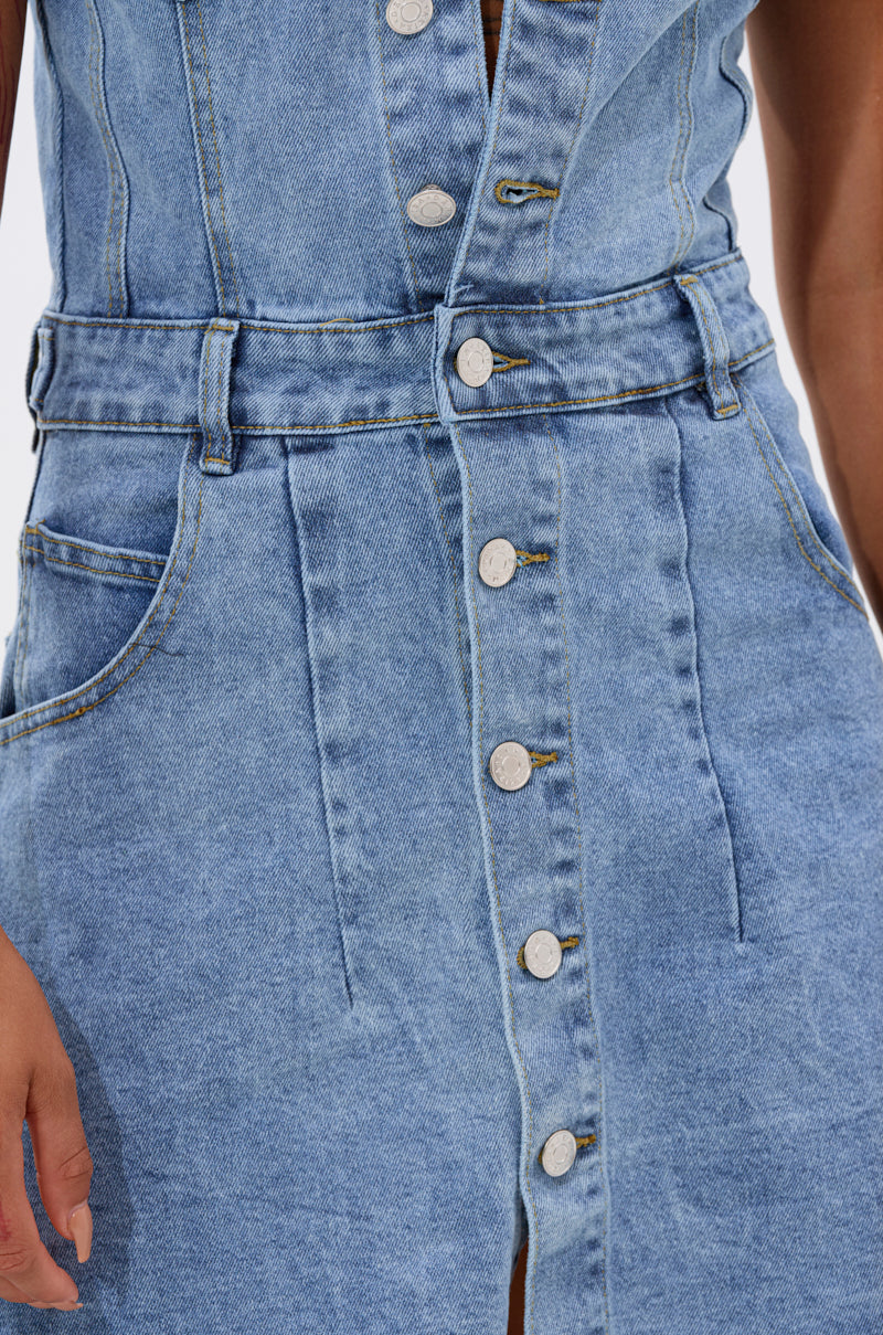 Close-up of a person wearing the READ IT AND WEEP DENIM MINI DRESS, featuring a light wash, silver buttons, belted waist, visible seams, side pockets, and a subtle ruffled hem. The left hand is partially visible on the image’s left side.