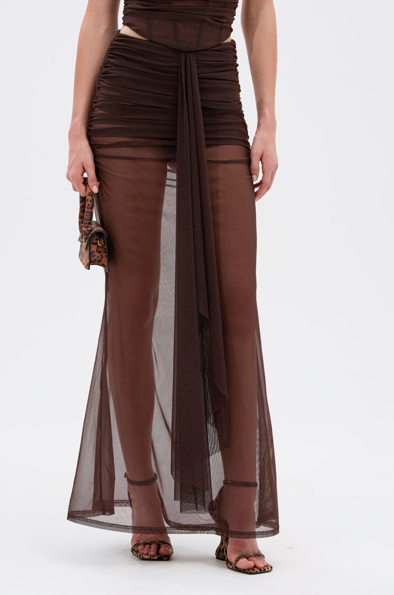 Wearing the SHAKE IT FOR ME GIRL MESH MAXI SKIRT—a sheer brown ruched mesh maxi with a draped front—this person pairs it with strappy heeled sandals and a patterned mini handbag. Photo is cropped at the shoulders. 2