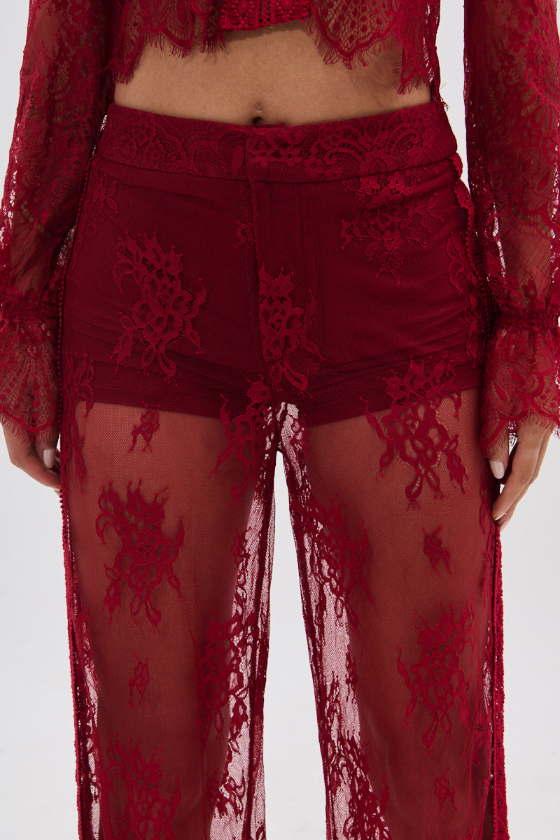 A person wears the LOVE LOST LACE PANT—high-rise, sheer red floral lace pants over matching shorts and a long-sleeved lace top—shown from waist to mid-thigh, with intricate patterns and a flattering fit.