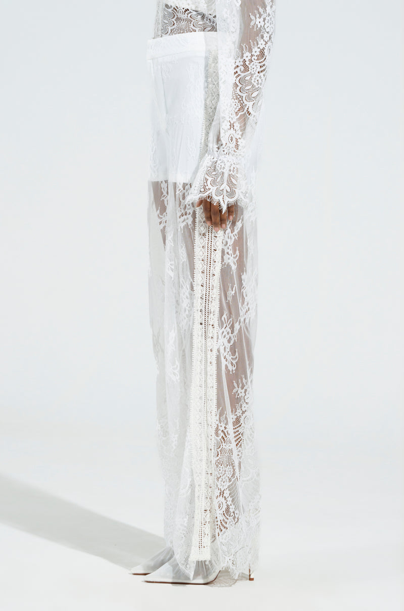 A model showcases the MISS ME YET LACE TROUSER, a sheer, floral lace design with high-rise elements, elegantly layered over a white undergarment against a neutral light background.