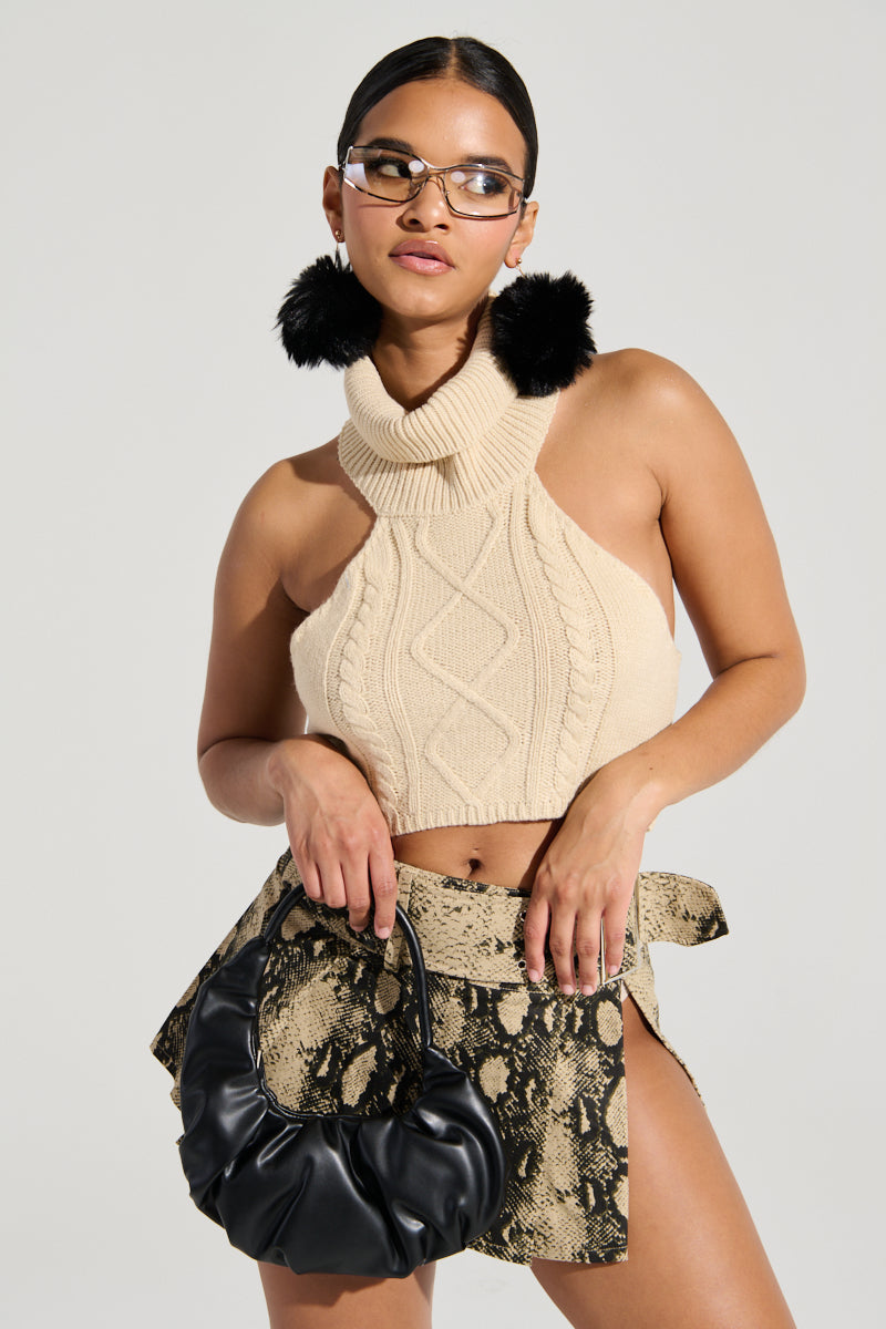 A woman stands confidently in the OUT OF HIS LEAGUE SLEEVELESS FASHION TOP, which adds depth with its textured panel design against the light gray background. She pairs it with a beige knit halter top and a snake-print skirt featuring a high slit, accessorizing her look with reflective sunglasses, black fur earrings, and a black handbag. Her hair is pulled back to complete the ensemble.