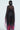 A person with straight black hair is seen from behind wearing THE JULIE BLOUSE—an elegant, long black gown with wide sleeves and a sheer pleated design that features a vibrant floral pattern at the bottom, creating a flowing effect.