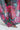 A sheer, colorful floral skirt billows gently, revealing silver strappy sandals and red-painted toenails on a light-colored floor; try swapping for THE JULIE TROUSER for an alternative look.