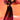 A woman poses against an orange backdrop in THE JULIE TROUSER—sheer black wide leg pants with vivid pink and purple florals. The high rise mesh and flowing silhouette add elegance as she raises her arms gracefully and turns her head.