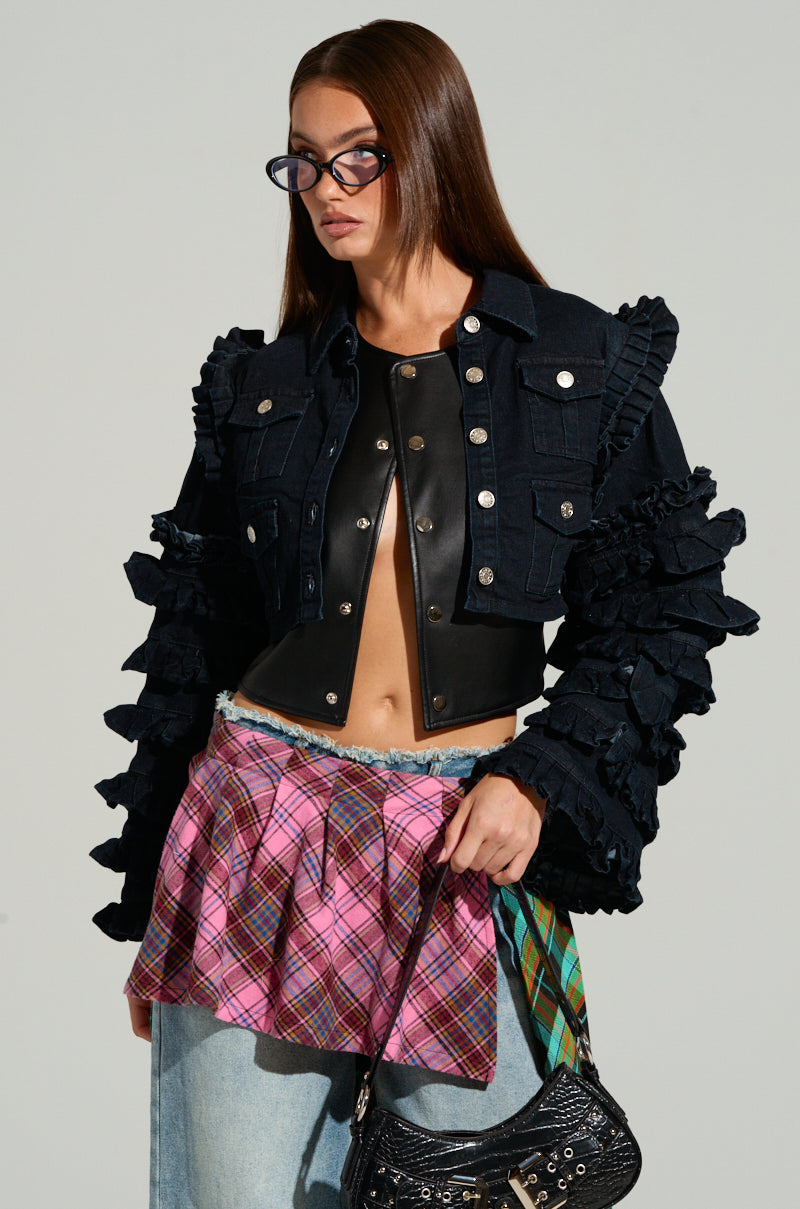 A person wearing the FELICITY STATEMENT SLEEVE DENIM JACKET, sunglasses, and a plaid pink skirt over denim pants holds a small black bag. They have long brown hair and a confident expression.