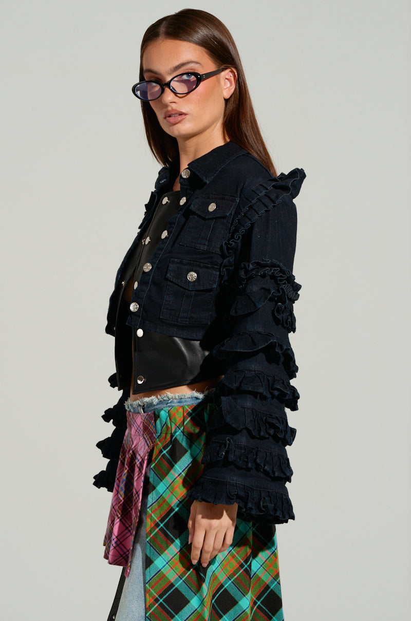 Dressed in the FELICITY STATEMENT SLEEVE DENIM JACKET, a person stands against a neutral background wearing a black denim jacket with striking sleeves paired with a patterned skirt. Their look is accentuated by dark-framed glasses, while their long brown hair cascades down as they gaze to the side.