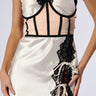 A person wearing the STRUCTURED QUEEN UNDERBUST BELT with a satin and lace lingerie dress. The cream-colored dress features contrasting black lace accents, a corset-style top with spaghetti straps, and an underbust belt for added definition. The lower part has lace-up detailing and black lace appliqués on one side.