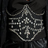 A person is dressed in a black outfit featuring a sheer mesh top with structured draping and shimmering embellishments, paired with black leather pants. The ensemble is adorned with intricate patterns of shiny, faceted gems and is complemented by the JODIE RHINESTONE BELT that adds an extra touch of sparkle.