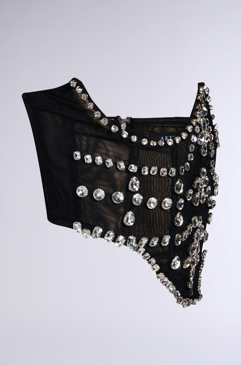 Introducing the JODIE RHINESTONE BELT, a stunning black sheer mesh corset top adorned with an array of sparkling rhinestones in a grid pattern. This underbust design showcases an asymmetrical style with a pointed hemline against a plain white background.