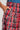 Close-up of a person's hand tucked into the pocket of a red and plaid skirt crafted from soft cotton. The skirt's tartan design features red, black, brown, and blue stripes. Above the waistband, you can see the upper part of high-rise wide-leg PLAID SWAGGER SLACKS peeking through.