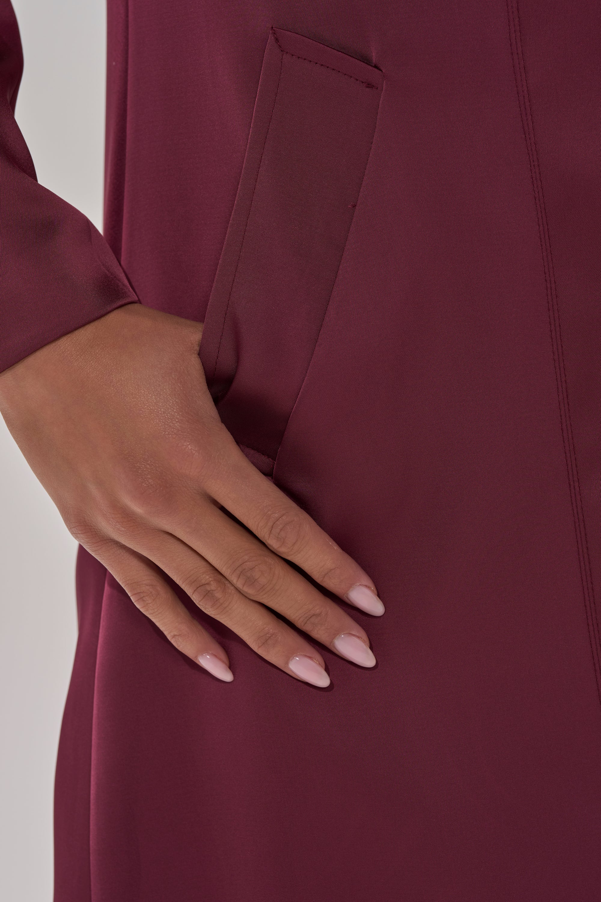 A close-up of manicured nails resting on the pocket highlights the elegance of the TAKE ME EVERYWHERE SATIN TRENCH IN BURGUNDY. 8