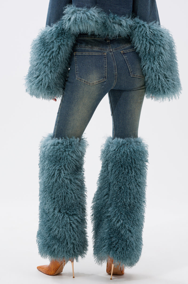 Model shown from the back wearing SIT PRETTY FUR TRIM JEANS IN BLUE DENIM, styled with blue furry leg warmers, a matching furry jacket, and tan high-heeled shoes against a plain white background.