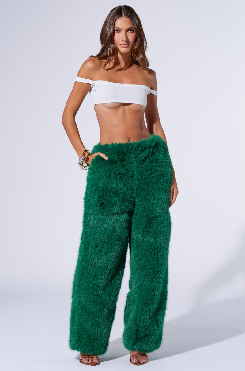 A woman with long, wavy hair is posing against a plain background, wearing a white off-the-shoulder crop top paired with the SEEING GREEN WIDE LEG FASHION FUR PANT. She has multiple bracelets adorning her right wrist.