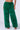 A person is modeling the SEEING GREEN WIDE LEG FASHION FUR PANT, made of vibrant and textured fluffy green faux fur. These high-rise, wide-leg pants stand out against the plain background. The person's midriff and arms are visible, and they are wearing strappy, open-toed sandals.