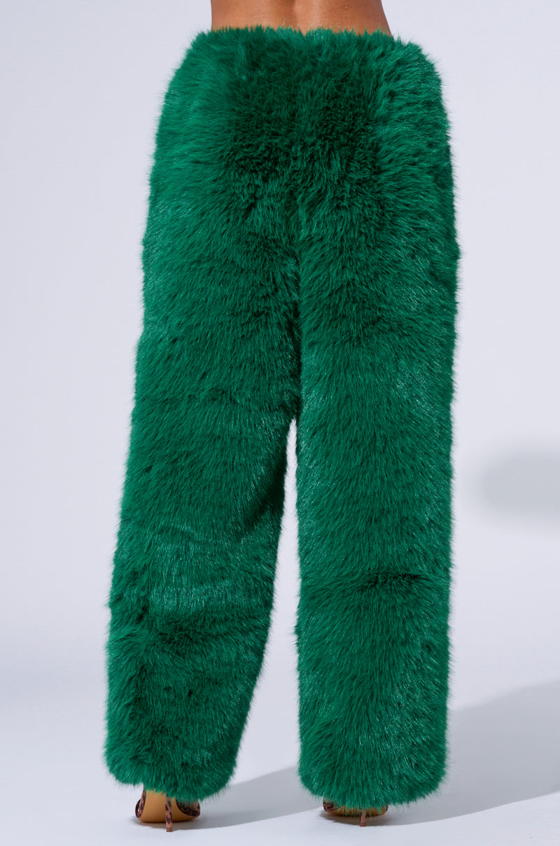 A person is wearing the SEEING GREEN WIDE LEG FASHION FUR PANT, which features high-waisted, wide-leg design in fluffy, bright green faux fur. The faux fur pants exhibit a soft, textured appearance as the person stands against a plain white background.