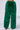 A person is wearing the SEEING GREEN WIDE LEG FASHION FUR PANT, which features high-waisted, wide-leg design in fluffy, bright green faux fur. The faux fur pants exhibit a soft, textured appearance as the person stands against a plain white background.