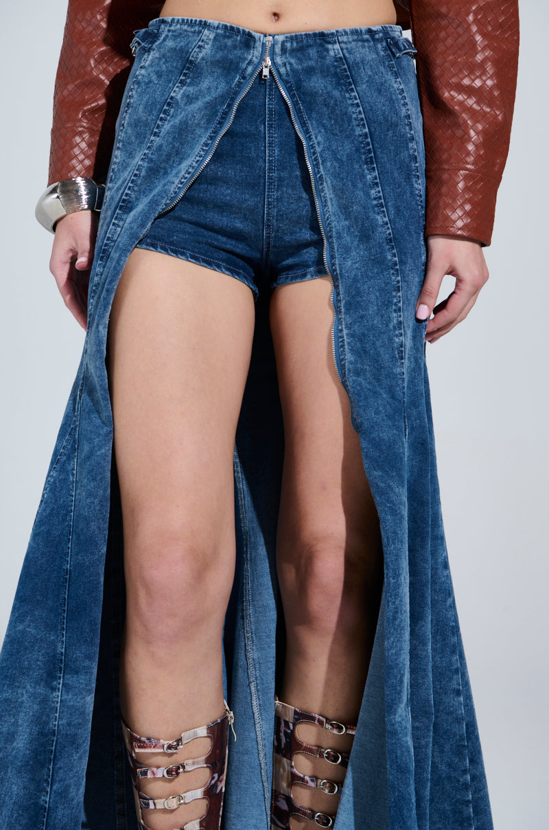 A person is styled in the Painted Lady Maxi Skirt with built-in shorts, giving off a denim maxi skirt vibe, accessorized with a textured brown jacket and a wide metallic bracelet, complemented by strapped high-heeled sandals.