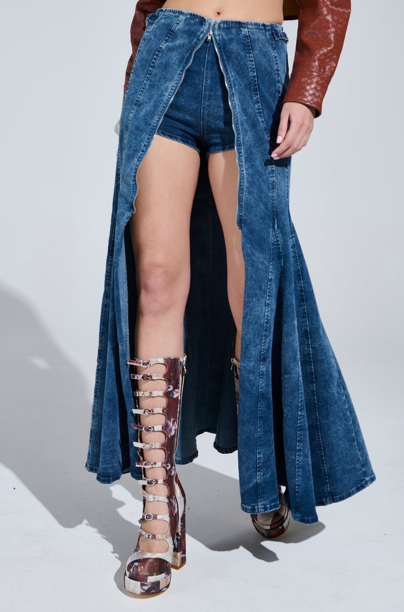 A person wears the PAINTED LADY MAXI SKIRT WITH BUILT IN SHORT, a stretchy blue denim skirt with high slits revealing matching shorts, paired with a brown textured long-sleeve top and knee-high strappy metallic platform boots for a fashion-forward look.