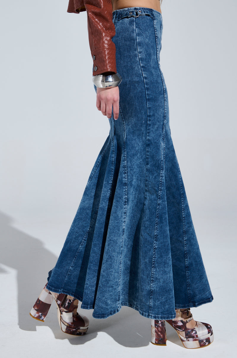 Styled in the PAINTED LADY MAXI SKIRT WITH BUILT IN SHORT, they pair it with a brown leather jacket and chunky platform sandals featuring a brown and beige pattern, presenting a bold fashion statement.