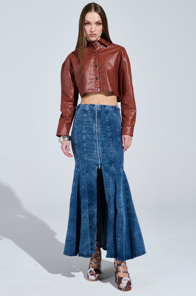 A person poses against a plain background, highlighting a brown textured crop jacket paired with the Painted Lady Maxi Skirt with Built-in Shorts in stretchy blue denim featuring front slits. They have long, straight hair and accessorize with heeled shoes.
