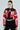 A woman with long hair, oversized glasses, and the ACE CROPPED GRAPHIC MOTO jacket from AKIRA Label pairs it with a black crop top and pants. Standing against a plain background, she exudes confidence as she looks directly at the camera.