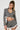 A person with braided hair wears a stylish SHORT N SWEET CROPPED BLAZER and shorts set, featuring white ruffles. The wool blend ensemble is accessorized with a large pearl necklace, and they hold a textured bag against a plain white background.