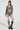 Clad in the chic SHORT N SWEET CROPPED BLAZER, a stylish wool blend blazer and matching skirt set with lace trim, a person strikes a confident pose. They pair the ensemble with thigh-high lace stockings and black platform boots, accessorizing with a beaded purse. Their hair is braided, complemented by bold jewelry.