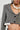 A person wearing the SHORT N SWEET CROPPED BLAZER, a wool-blend herringbone jacket featuring ruffle cuffs and black buttons. They have long braided hair and are adorned with a large pearl necklace. The plain background accentuates the outfit's intricate details.