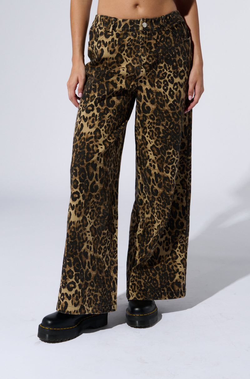 A person wearing the CHEETAH SISTERS PANT, featuring a wide-leg silhouette, paired with black platform shoes stands against a plain white background. The photo is cropped from the shoulders down, highlighting the distinctive pants and stylish shoes.