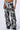 A person is shown wearing the GET WITH IT CARGO PANT, which features a black and white tie-dye design with a high rise waist and multiple pockets. These loose-fitting pants showcase an abstract painterly patterning and are paired with chunky black shoes. The photo is cropped at the waist, focusing on the pants and shoes.