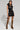 A woman is posing confidently in a trendy leather vest paired with the BACK TO THE FUTURE MINI SKIRT. She completes the look with knee-high leopard-print boots and a matching small handbag, her hair styled sleekly back.