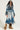 Dressed in the LIV FUR TRIM DENIM TRENCH featuring a luxurious fur-trim collar and cuffs, a person confidently strikes a pose against a plain background. Oversized sunglasses complement the ensemble, while fuzzy brown boots complete the look. The coat's belted waist adds an extra touch of flair to their outfit.
