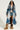 A person dressed in the LIV FUR TRIM DENIM TRENCH pairs it with denim shorts and a black top. They confidently accessorize with dark sunglasses, a handbag, and complement their look with fur boots.