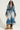 A person confidently stands wearing the LIV FUR TRIM DENIM TRENCH, featuring a chic fur trim collar and cuffs. They have long, curly hair and sport trendy sunglasses. Their outfit is completed with fur boots, and they carry a small bag.