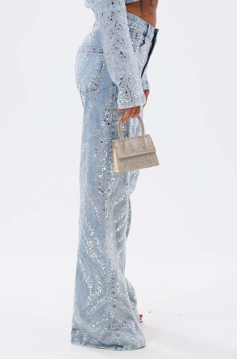 A person wears the DIAMONDS DANCING DENIM FLARE PANT—light blue, high-waisted, jeweled flare jeans—with a matching cropped jacket and a small glittery gold handbag against a plain white background.