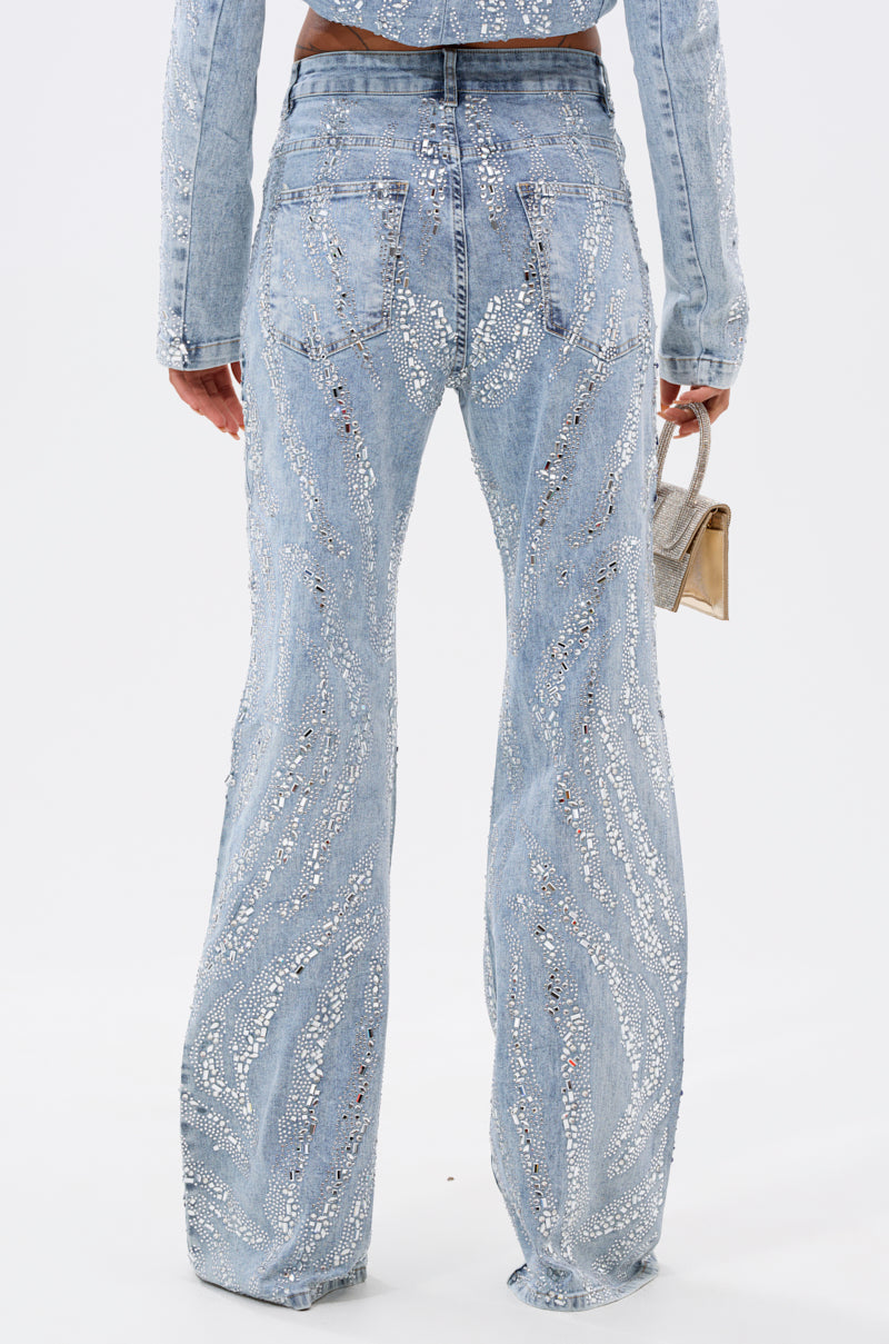 A model shown from the back wears the DIAMONDS DANCING DENIM FLARE PANT—light blue, high-rise flares with sequins—paired with a fitted jacket and small metallic purse against a plain white background.